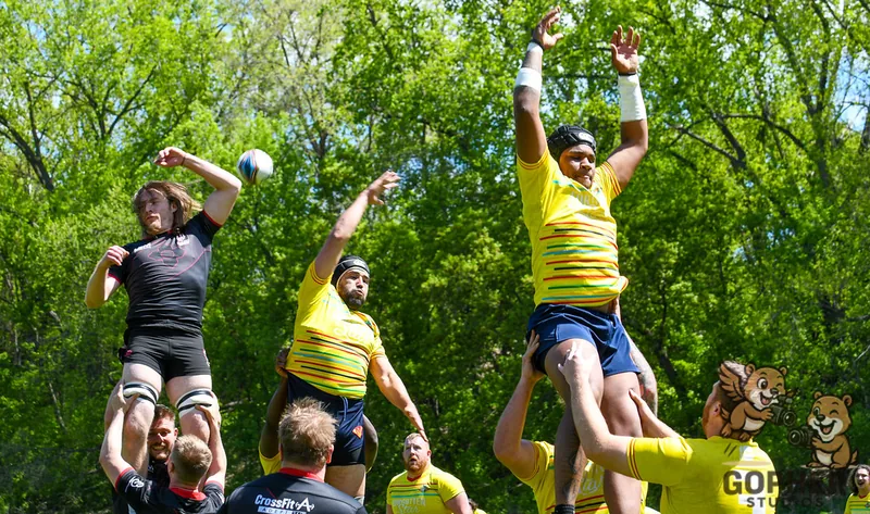 Rugby players in black and yellow are lifted by teammates to contest a lineout.